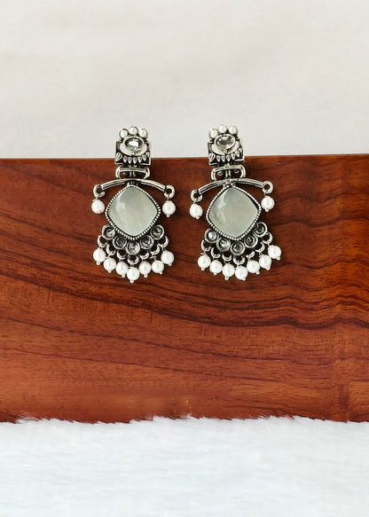 A pair of silver-toned traditional Indian chandbali earrings with oval light green stones and small white bead drops, displayed on a wooden block against a white background.