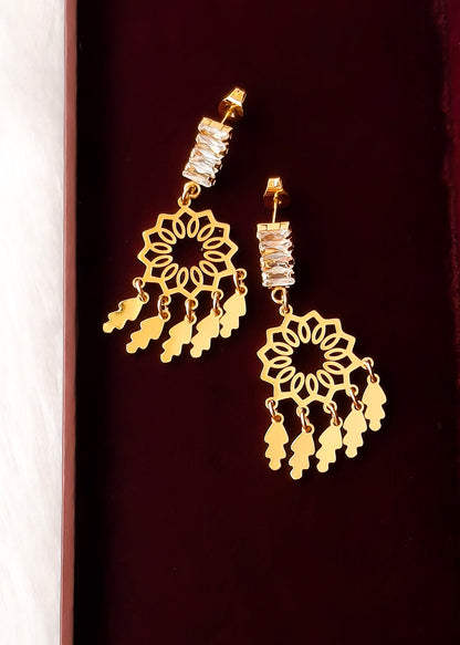 A pair of gold-toned dangle earrings with intricate filigree cutouts, clear rhinestone-studded posts, and dangling leaf-shaped charms, displayed on a dark burgundy background.