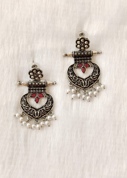 A pair of traditional Indian silver-toned dangle earrings with red floral accents and white pearl bead drops, displayed on a textured white fabric background.