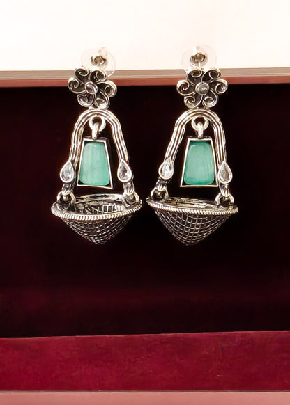 A pair of silver-toned traditional Indian earrings with rectangular mint green stones, displayed in a dark red velvet jewelry box.