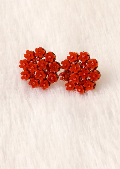 A pair of red floral stud earrings with small faceted clear stones, displayed on a white faux fur surface.