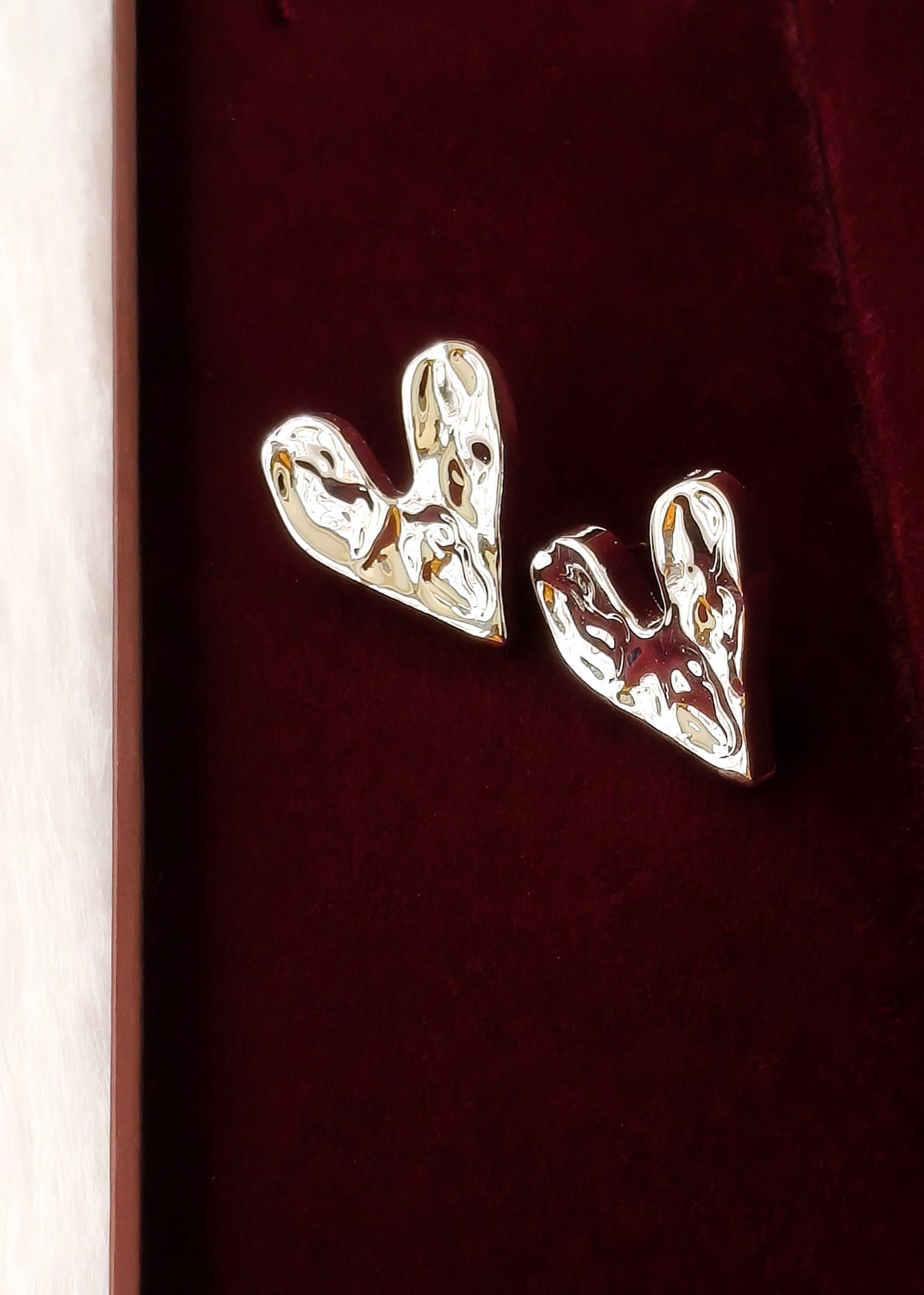 A pair of polished silver heart-shaped stud earrings resting on a deep burgundy velvet surface.