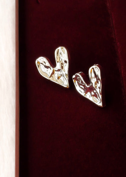 A pair of polished silver heart-shaped stud earrings resting on a deep burgundy velvet surface.