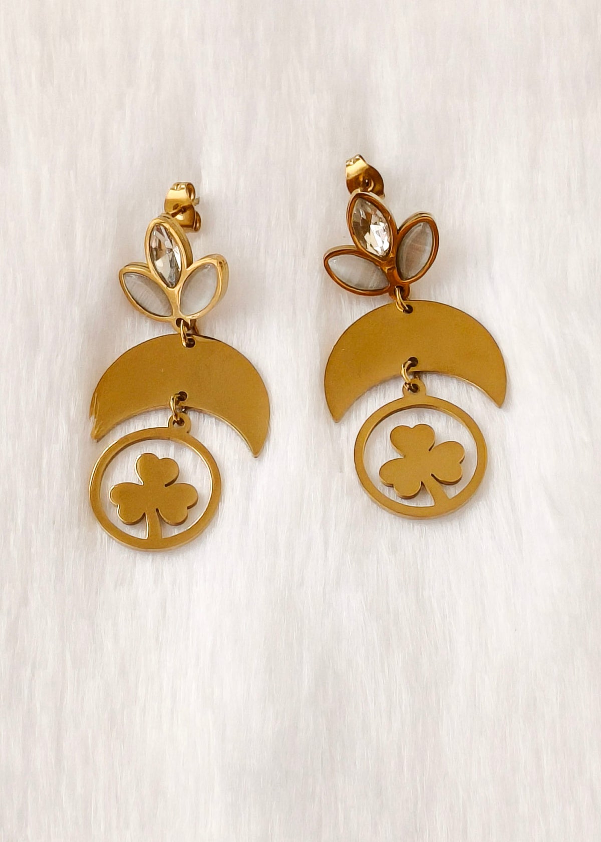 A pair of gold-toned dangle earrings with crescent moon, shamrock, and leaf motifs, displayed on a light textured background.