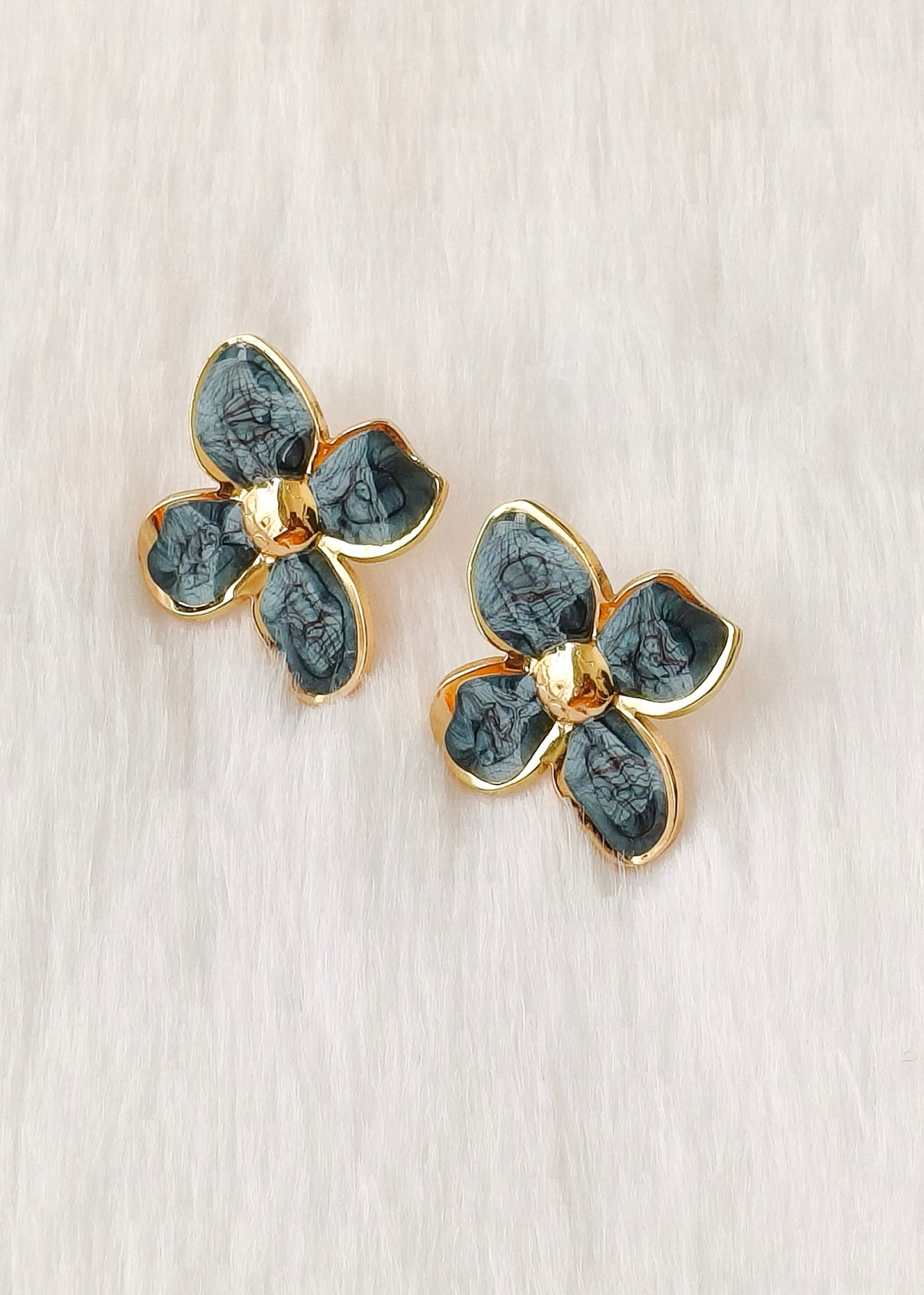 A pair of gold-tone flower-shaped earrings with textured dark green enamel petals, displayed on a light beige textured surface.