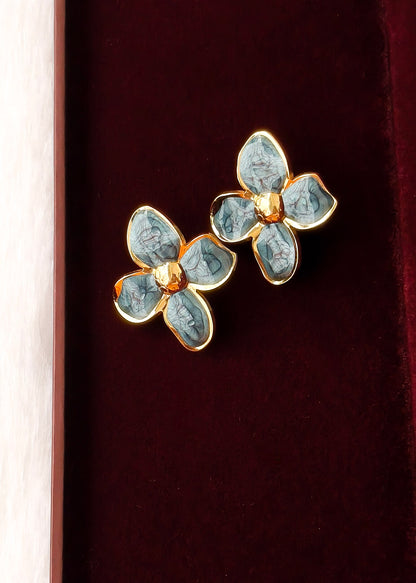 A pair of gold-tone flower-shaped earrings with light blue enamel petals, displayed on a dark red velvet surface.