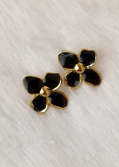 A pair of black and gold flower-shaped stud earrings on a textured white background.