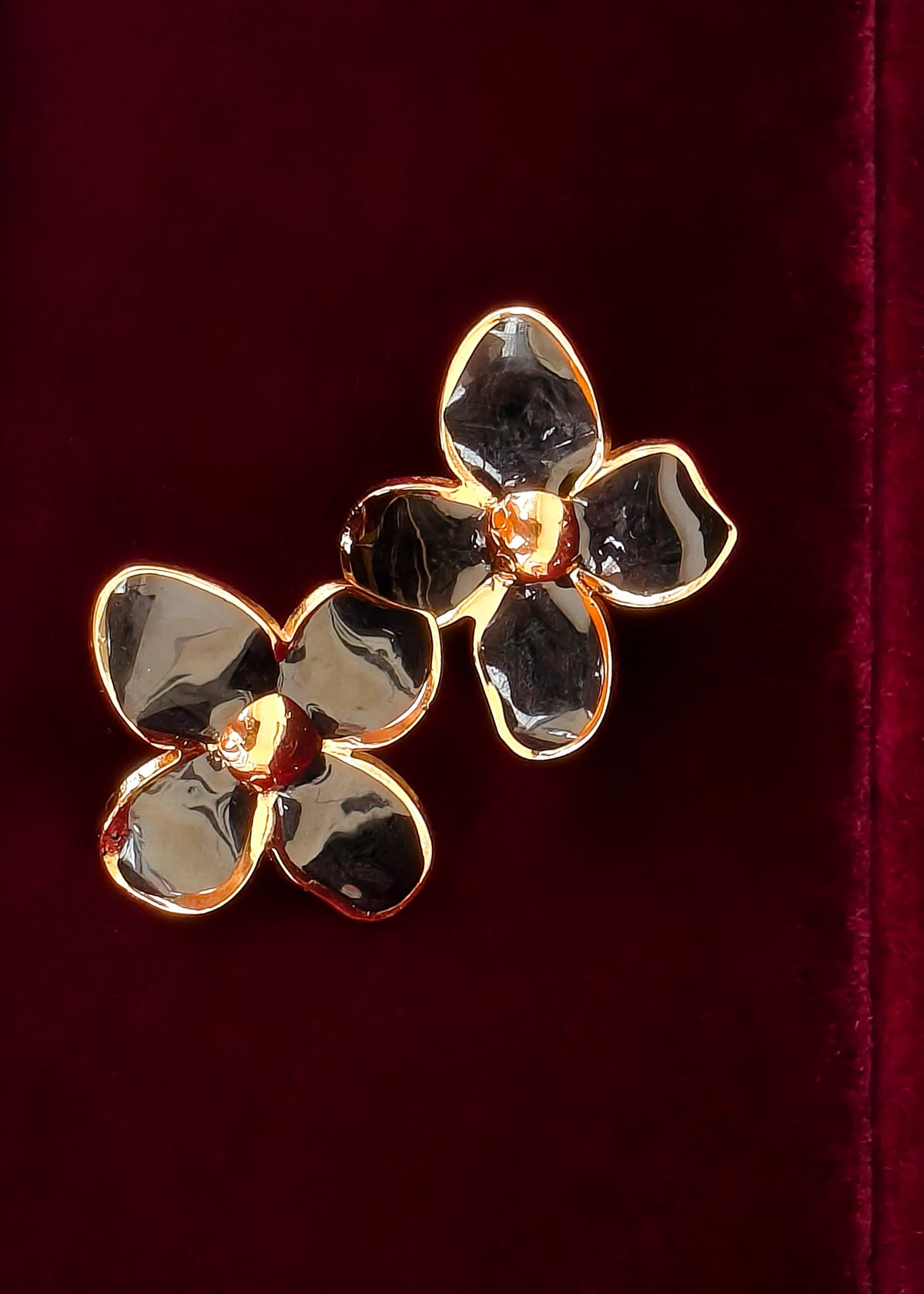 A pair of gold flower-shaped earrings with textured, hammered metallic petals, displayed on a deep burgundy velvet background.