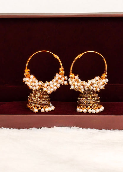 A pair of traditional Indian gold jhumka earrings adorned with white pearls, displayed on a dark brown velvet jewelry box.