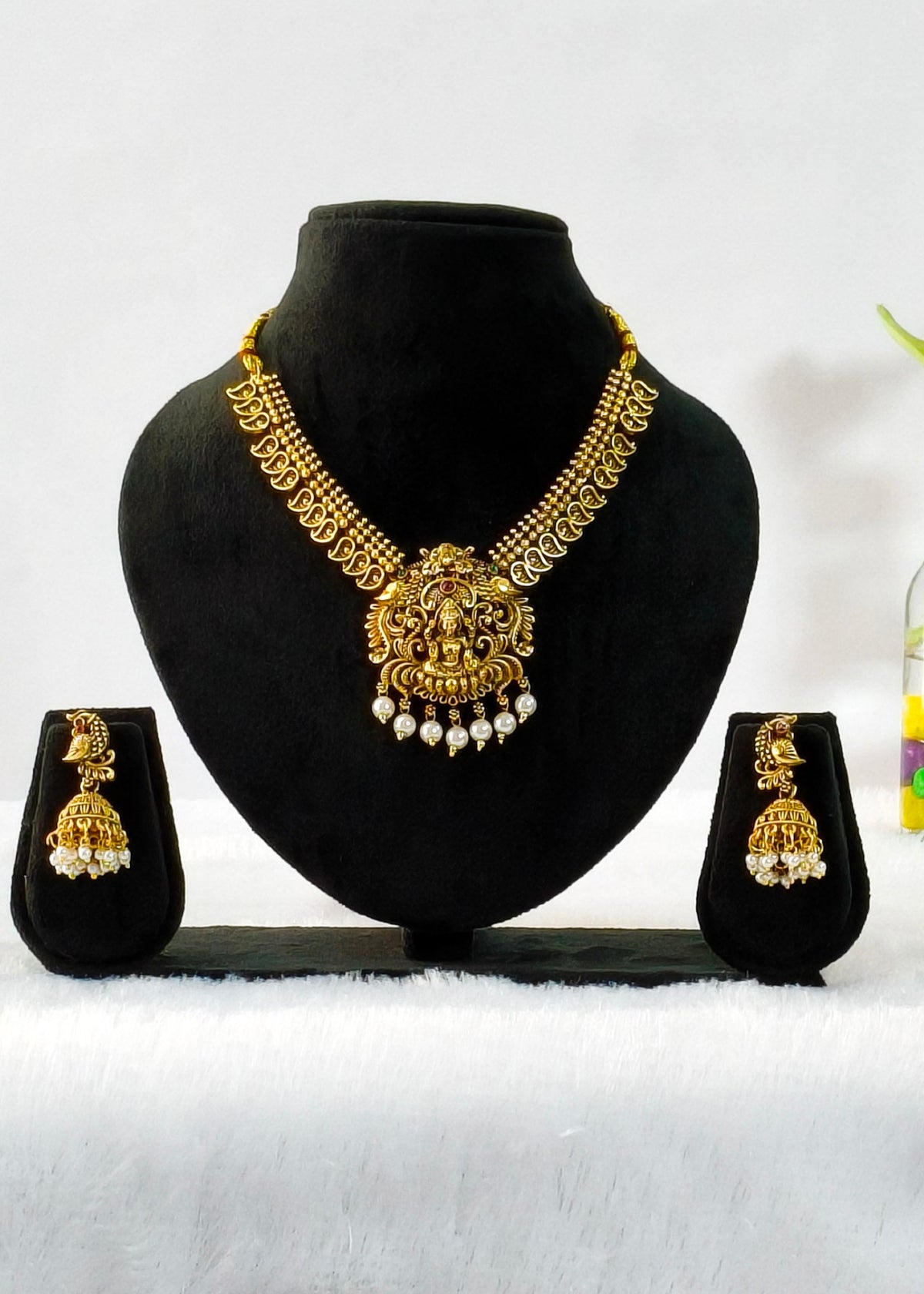 Rukmini leaf-motif Lakshmi necklace with pearl drops and matching peacock jhumkas on a black display.