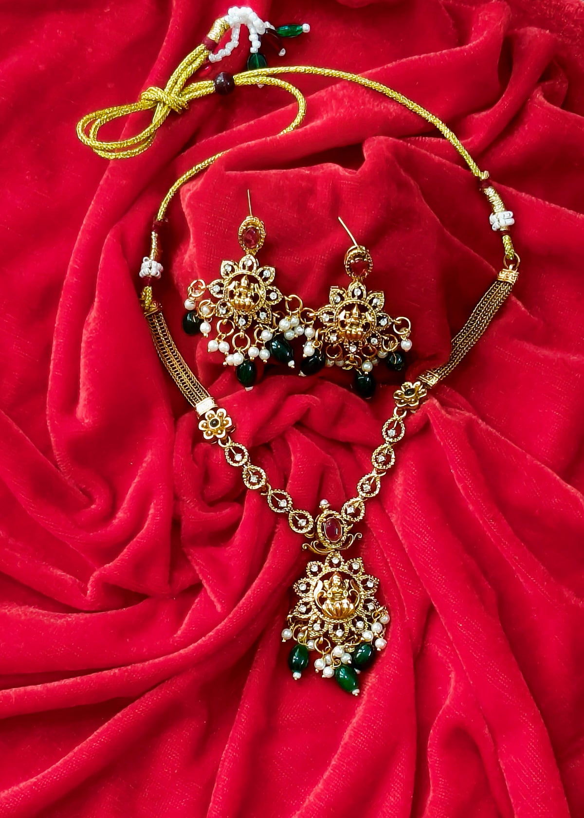 Vidya Lakshmi necklace set on red fabric, showing matching earrings, pearl clusters, green drops and adjustable tie cord.