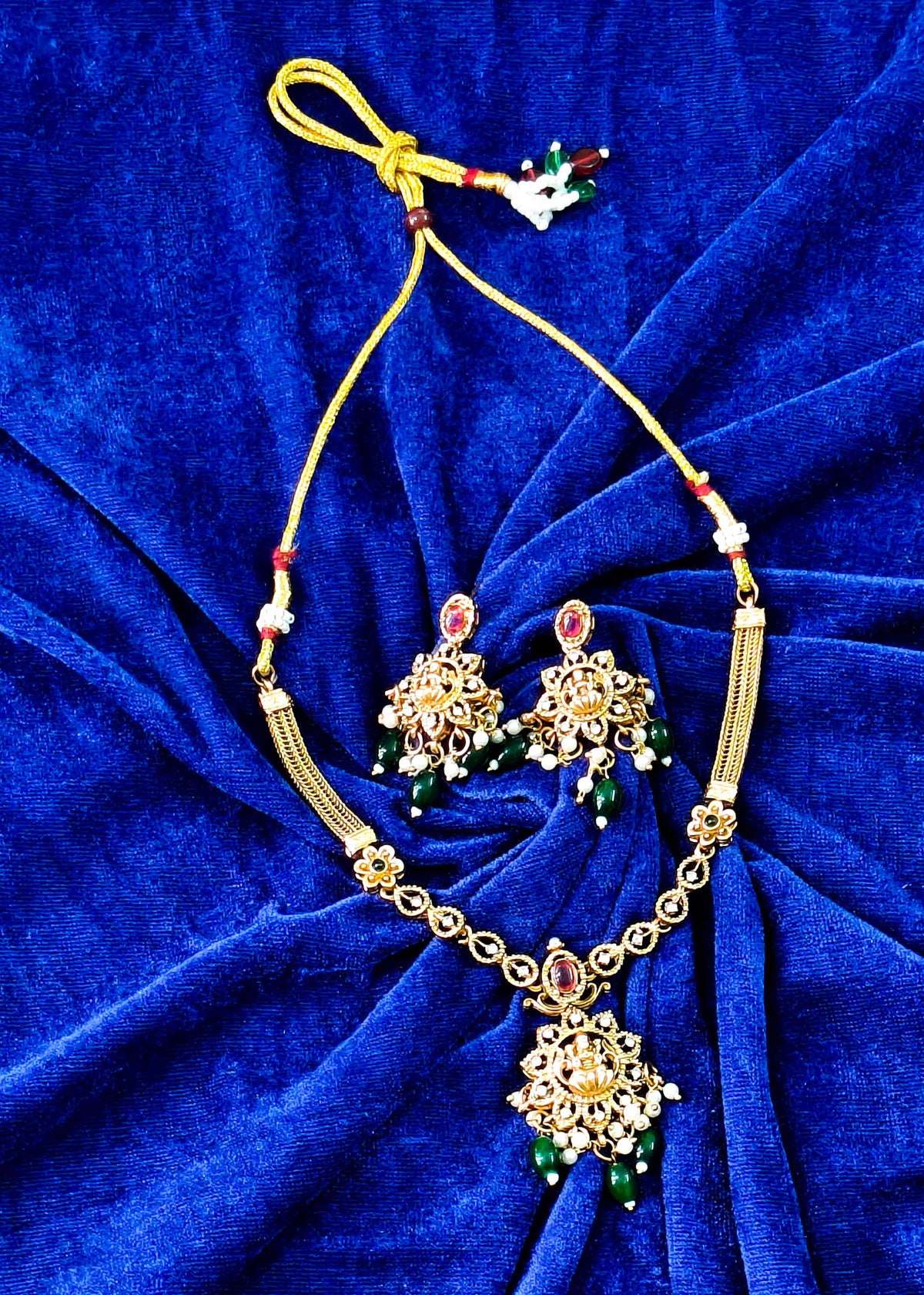 Vidya temple necklace and earrings on blue fabric, with Lakshmi motifs, red stones, green drops and pearl clusters.