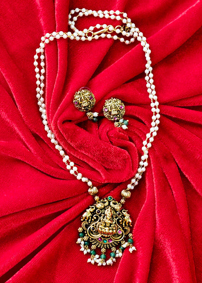 An ornate gold-toned necklace with a detailed pendant and matching stud earrings, arranged on a bright red velvet fabric background.