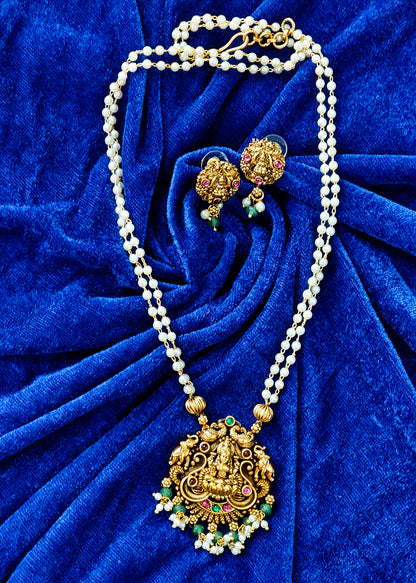 Gold and white pearl jewelry set featuring a traditional pendant necklace and matching earrings, displayed on a textured royal blue velvet background.