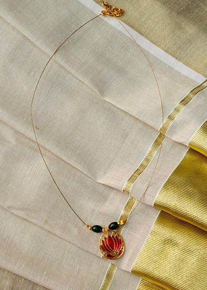A delicate gold necklace with a lotus pendant, accented by two small black beads, displayed on a draped cream-colored fabric with gold borders.