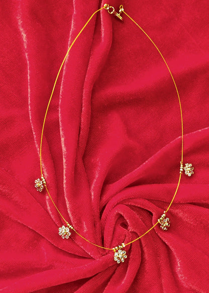 A delicate gold necklace with small floral cluster charms, displayed on a vibrant red textured fabric background.