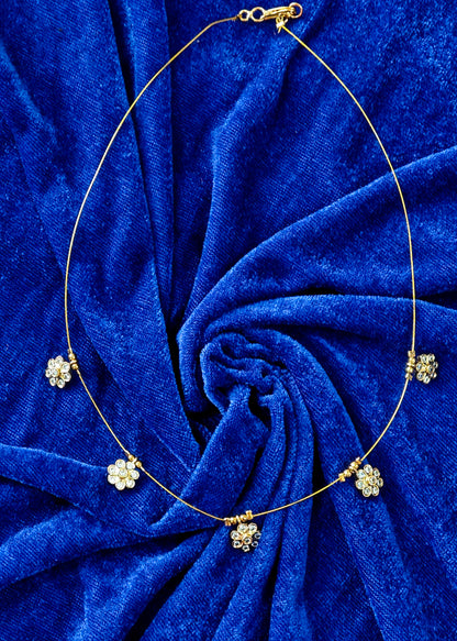 A delicate gold chain necklace with five small floral clusters of clear rhinestones, displayed on a textured royal blue velvet fabric background.