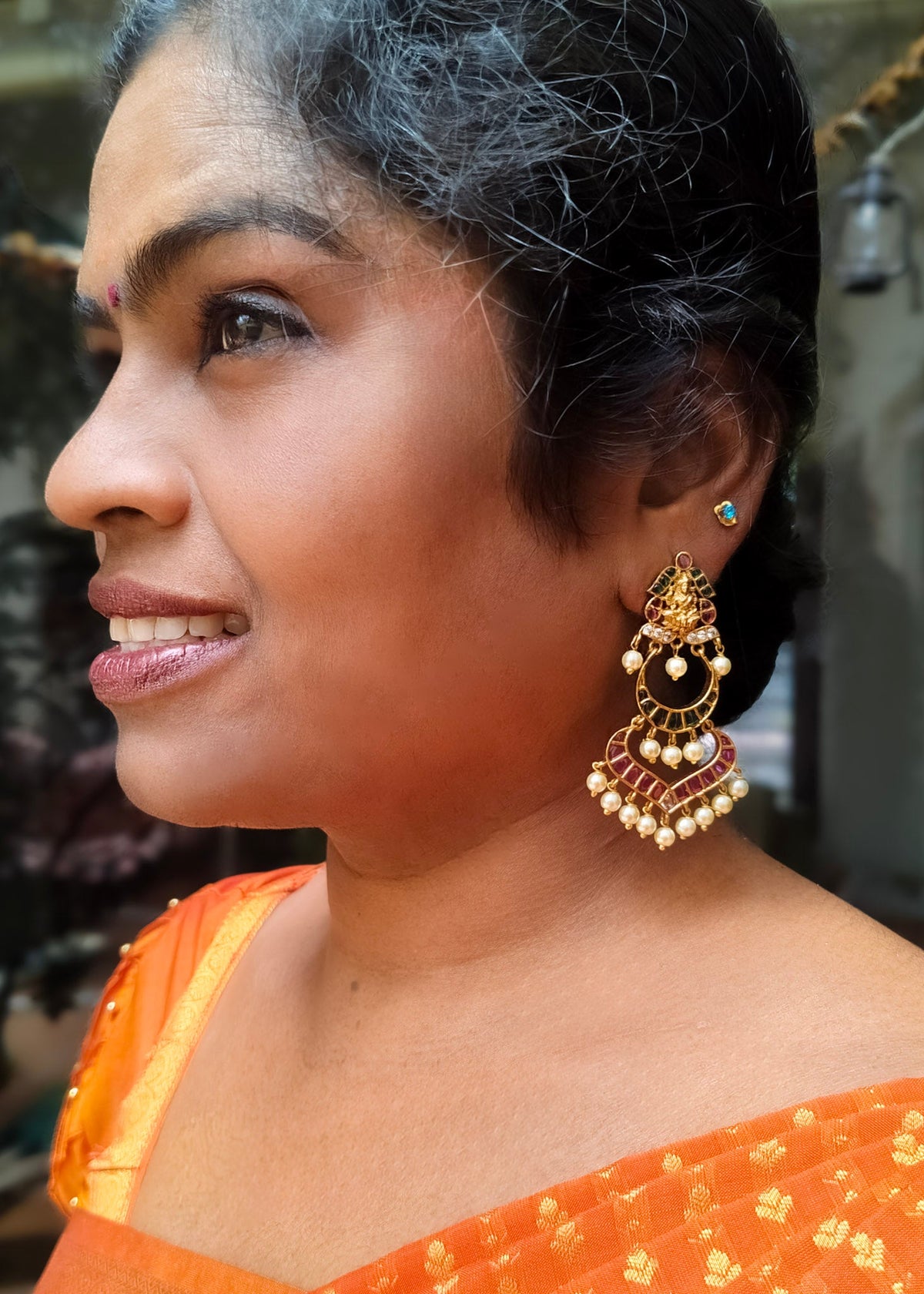 A woman in profile wearing a large ornate gold-toned traditional jhumka earring with black and white bead detailing.