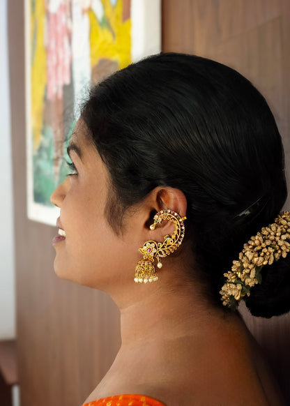 A woman in profile wearing ornate gold traditional earrings with dangling jhumka-style elements.