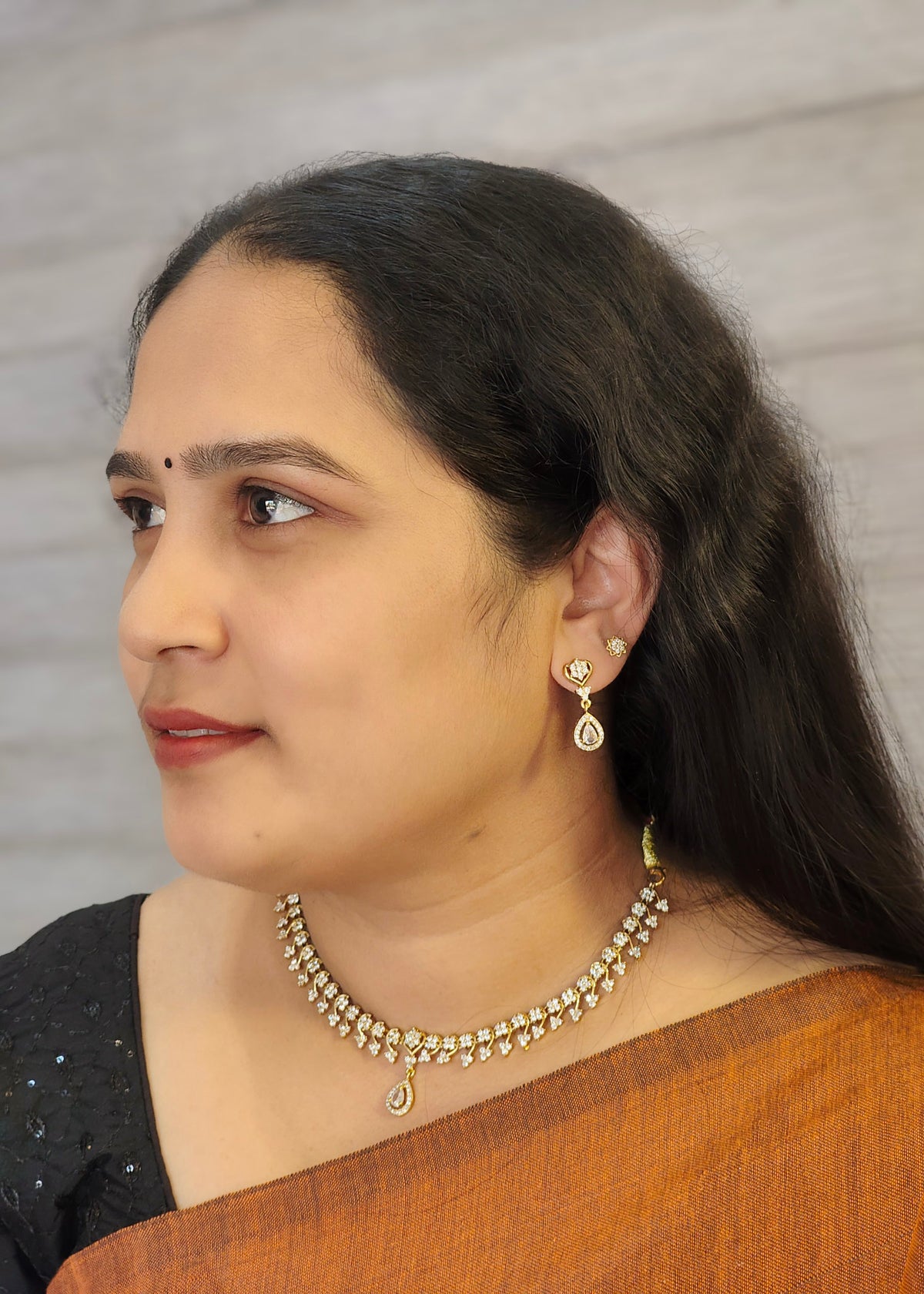 A woman in profile wearing a gold-toned American diamond necklace and matching drop earrings.
