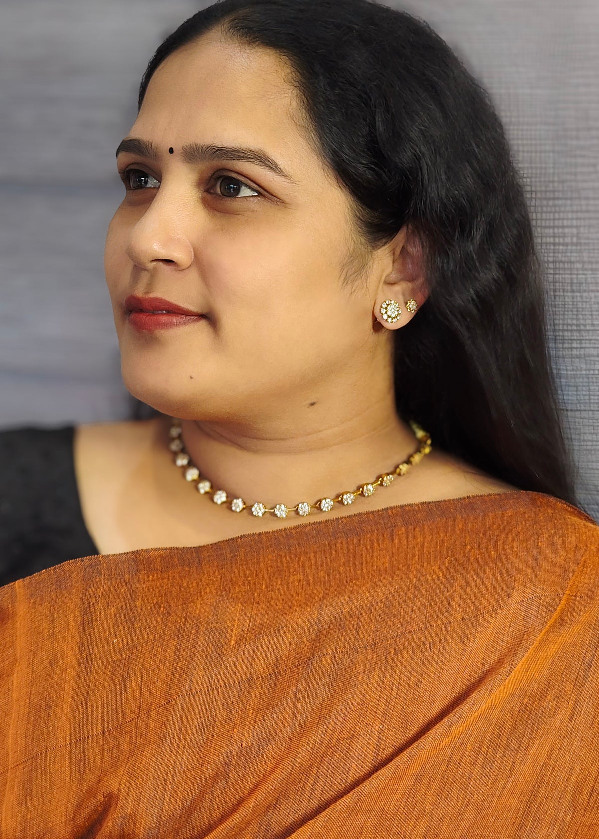 A woman wearing a gold-toned American diamond necklace and matching stud earring, 