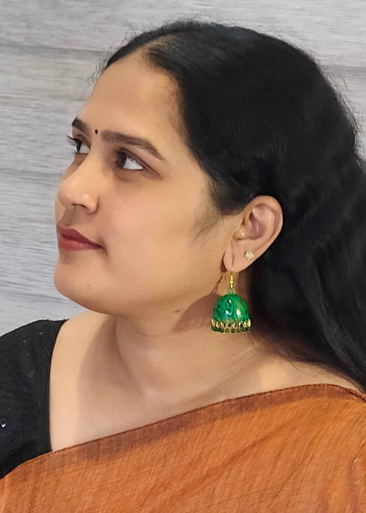A woman wearing a pair of green and gold jhumka earrings, 