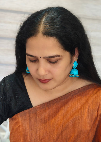 A woman wearing a brown and black saree and bright blue jhumka earrings, 