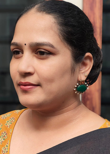 A woman with dark hair tied back, wearing  a green teardrop earring, shown in a close-up portrait.