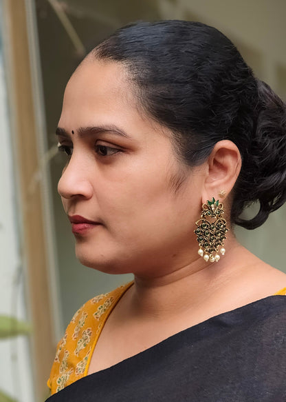 A woman in profile wearing a black saree with a  gold-toned earring with green stones.