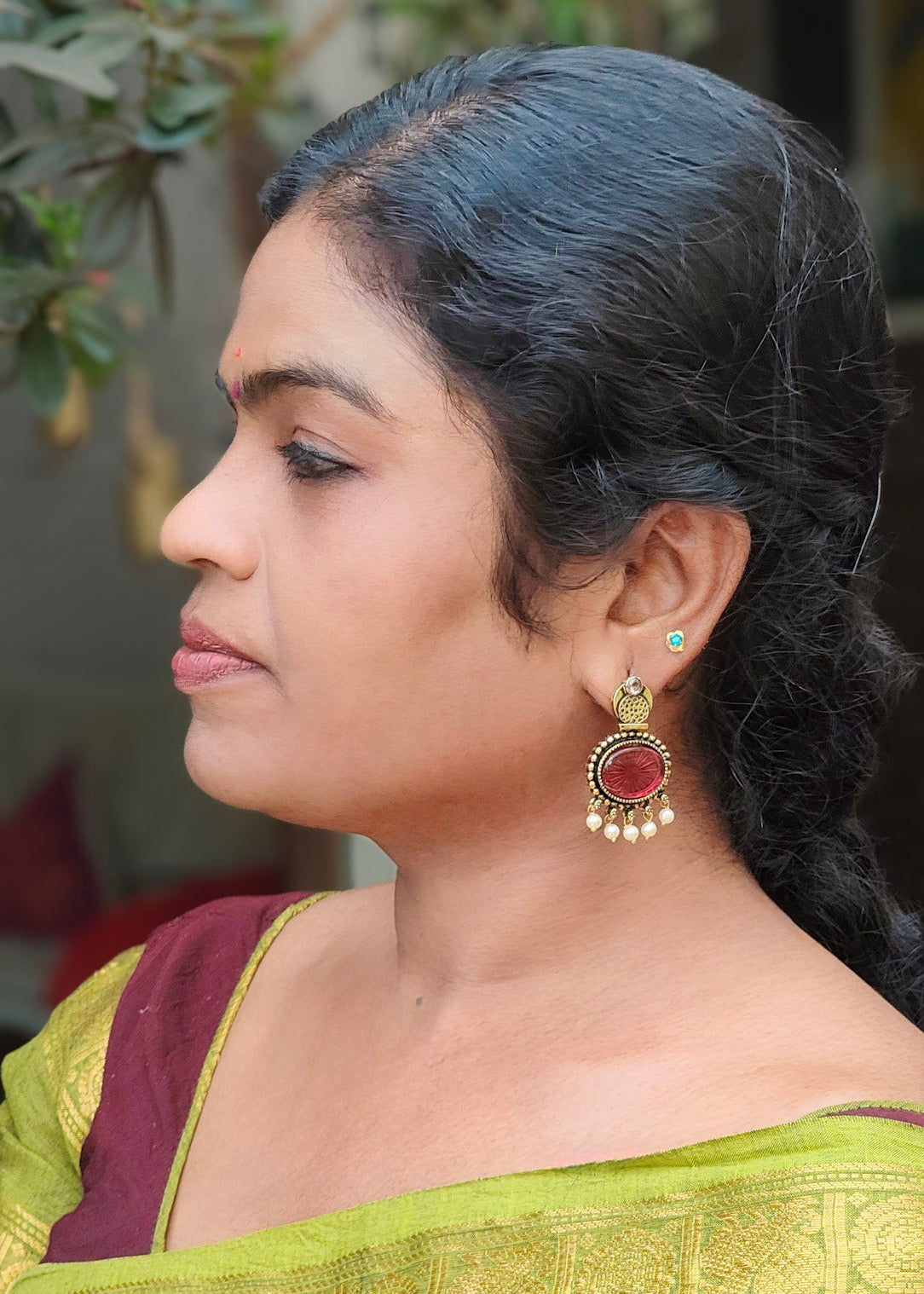 A woman in profile wearing  a gold and red dangling earring