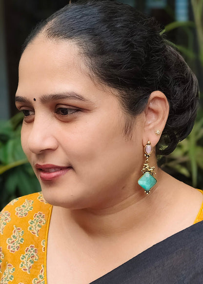 A woman wearing a black saree and gold earrings with turquoise-colored stones, shown in a close-up portrait.