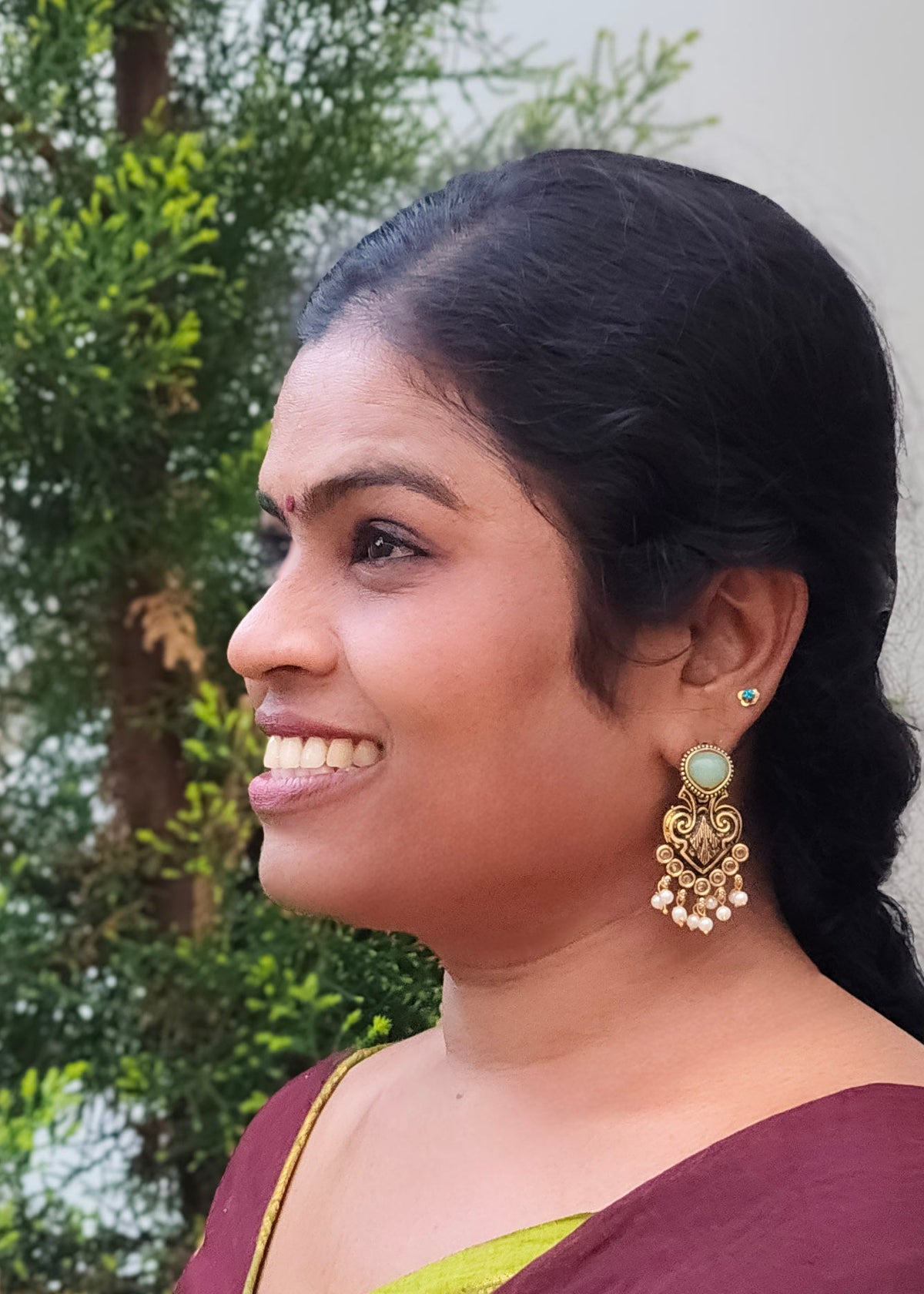A woman in profile wearing a gold-toned jhumka earring with a light green stone, 