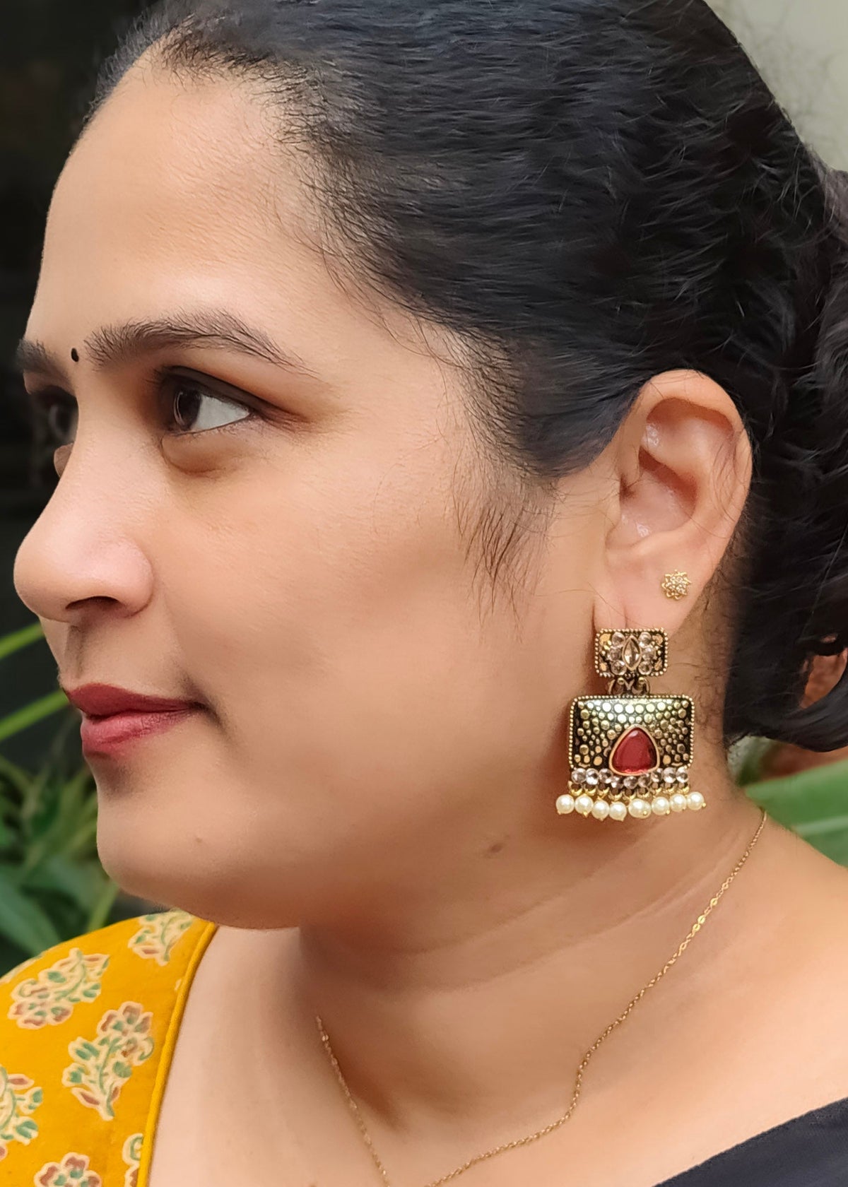 A woman in profile wearing a large ornate gold-toned jhumka earring with a red stone and white pearl border, 