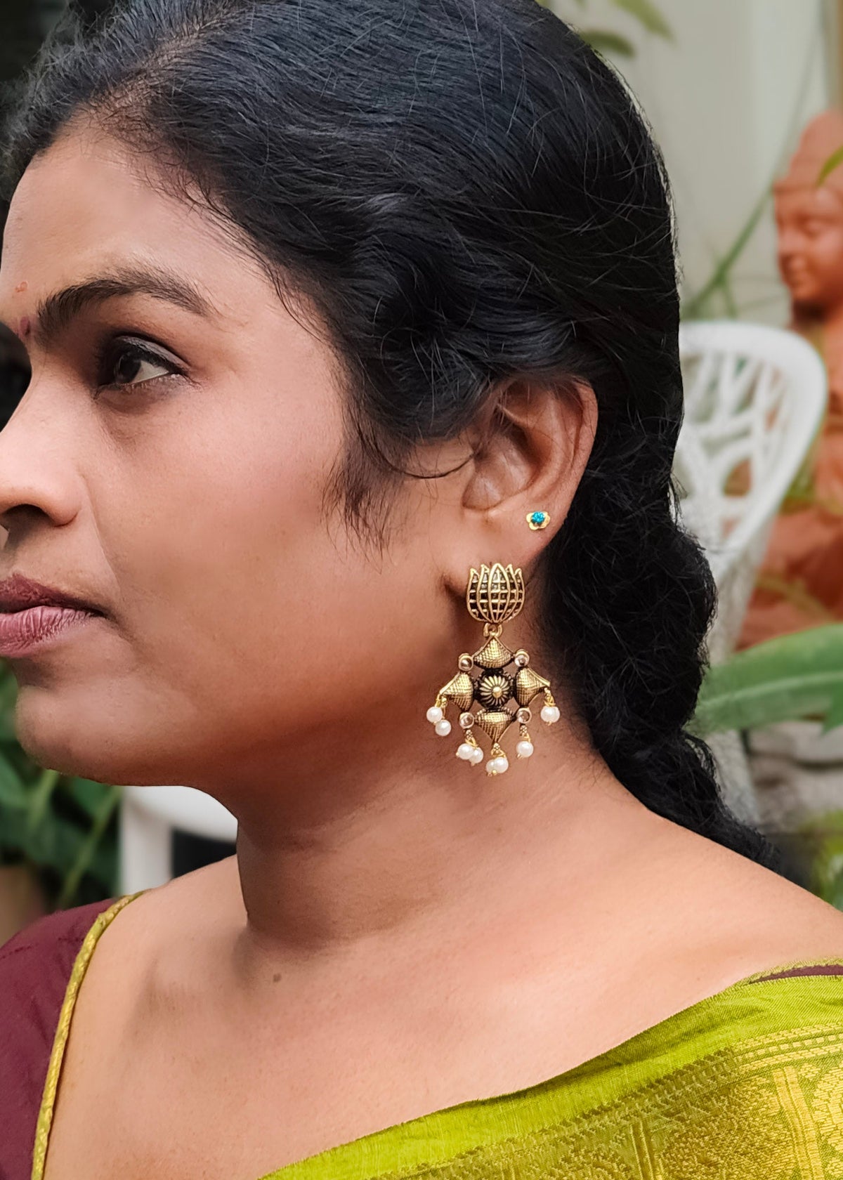 A woman in profile wearing a large gold-toned traditional jhumka earring with dangling pearl-like beads.