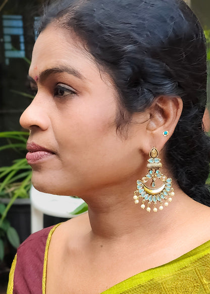 A woman in profile wearing a large gold-toned traditional jhumka earring with light blue stones and white pearl-like dangling beads, 