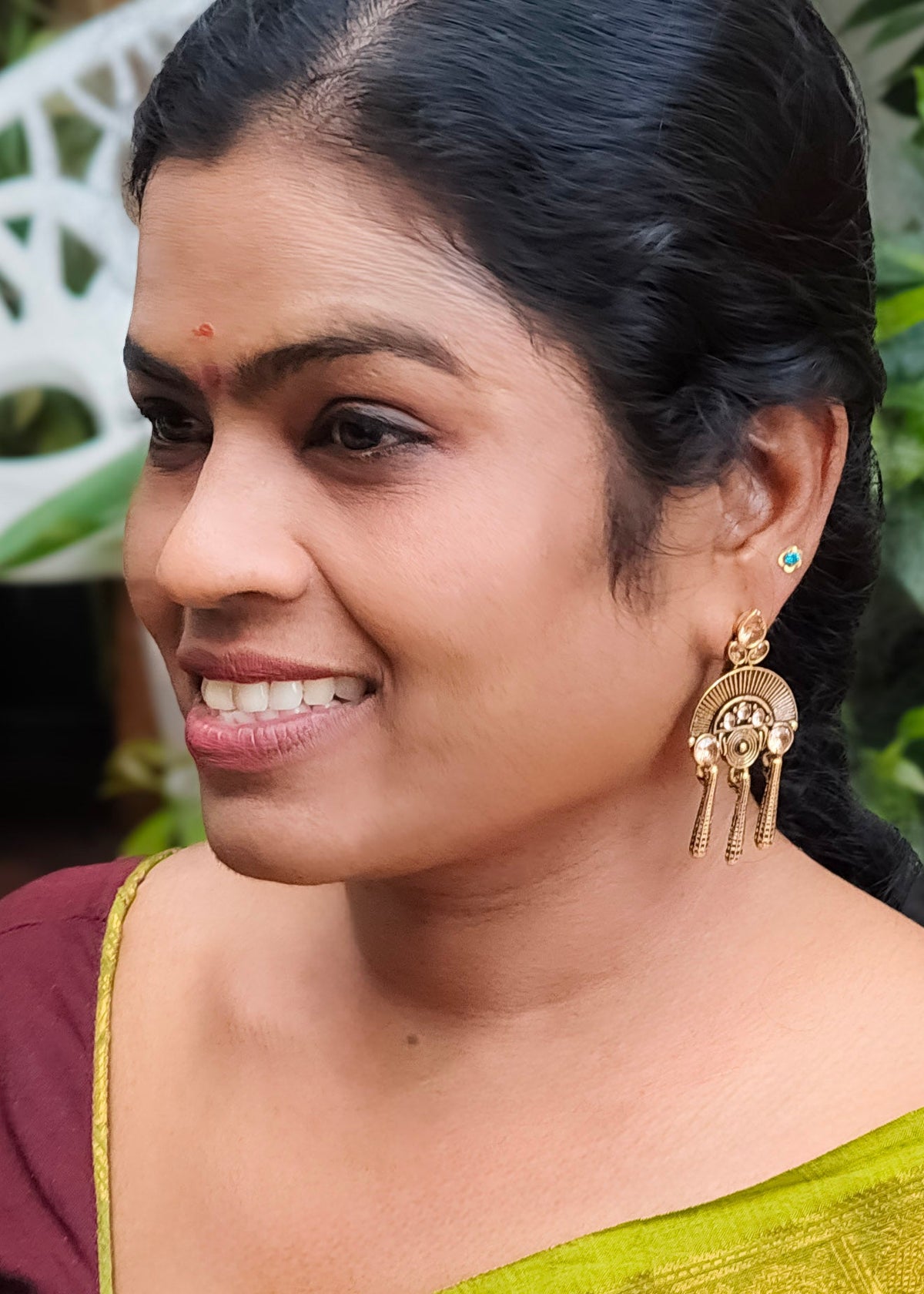 A woman in profile wearing a gold-toned traditional Indian earring with dangling tassels.