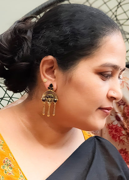 A woman in profile wearing a gold-toned traditional earring with dangling tassel details.