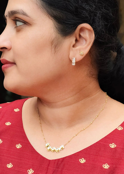 A close-up side profile of a woman wearing a red embroidered top, a delicate gold necklace, and a matching small gold stud earring.