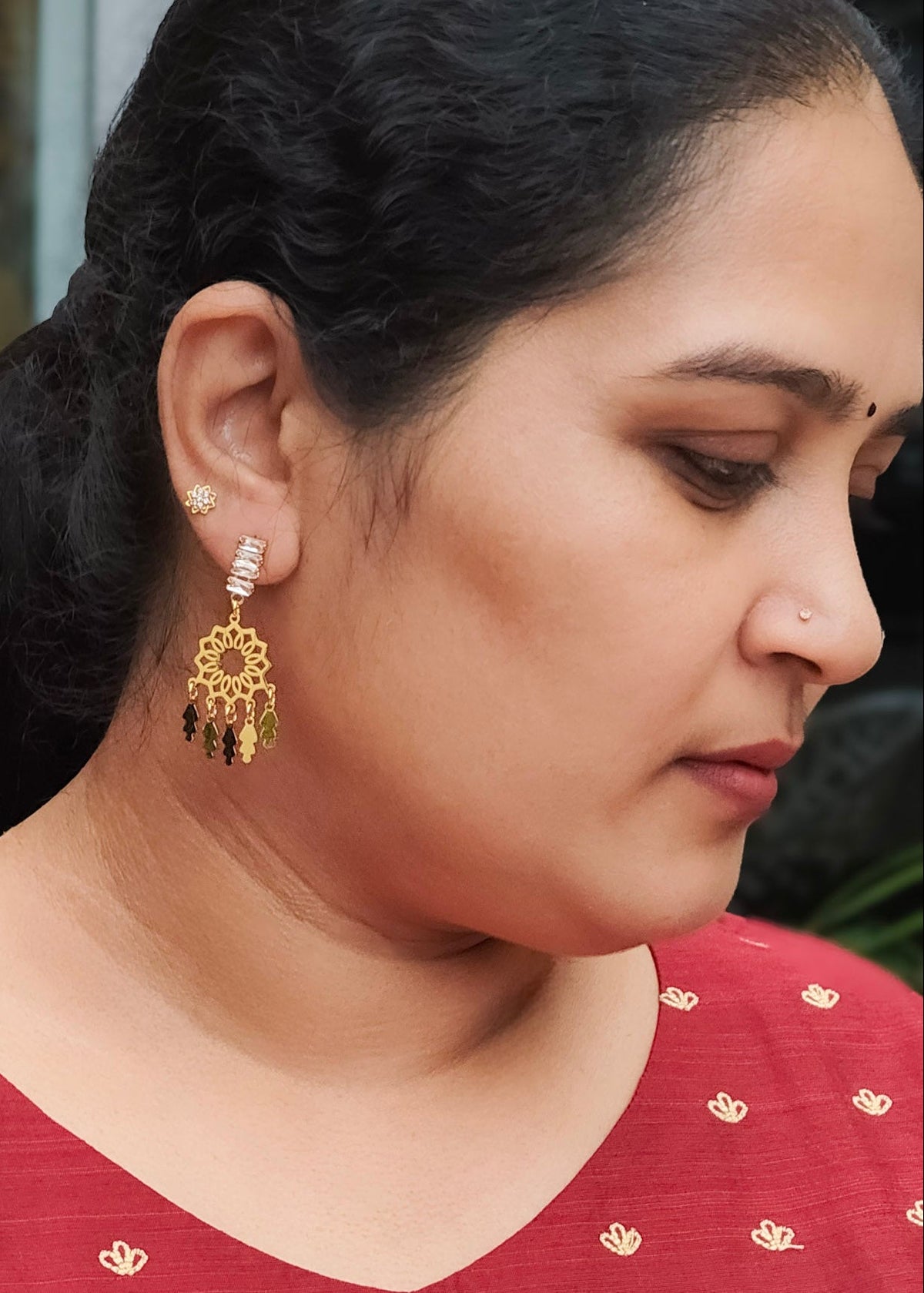 A woman wearing a gold-toned, multi-tiered chandelier earring with black dangling beads.