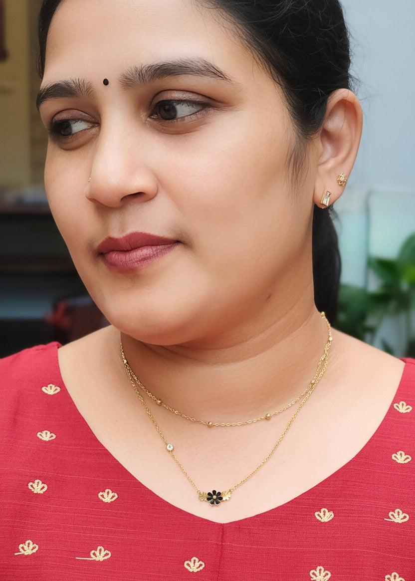 A close-up shot of a woman wearing a delicate anti tarnish gold layered necklace with a small black and gold flower pendant, 