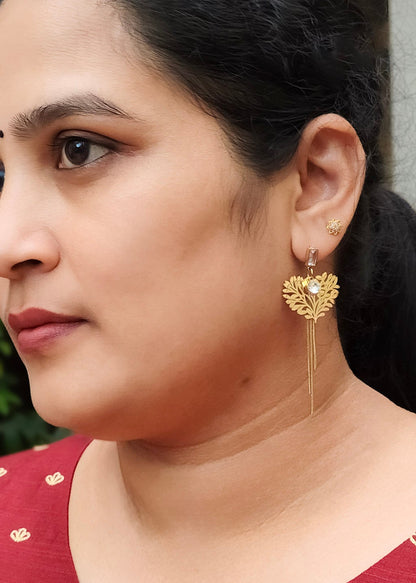 A woman wearing a gold heart-shaped dangle earring with a small clear stone.
