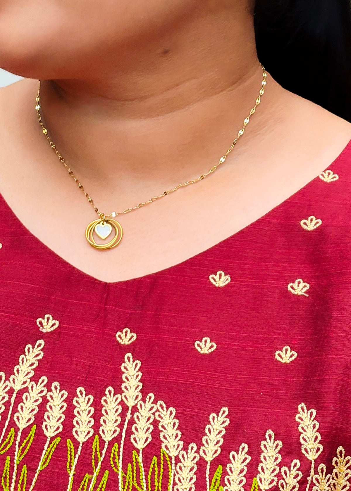 Woman wearing a gold plated anti tarnish necklace with multiple rings and heart pendant.