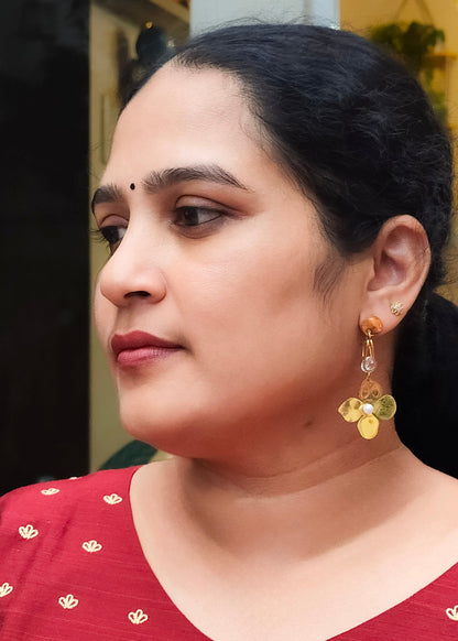 A woman wearing a red top with small gold motifs and a gold dangle earring with clear and gold beads.