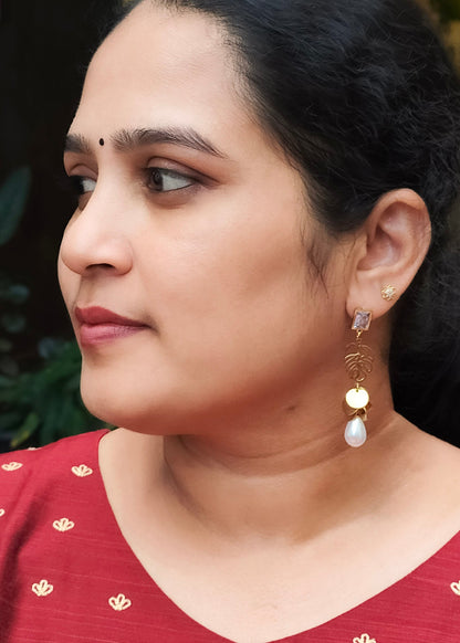 A woman wearing a red top with small gold motifs and a gold and white dangle earring.