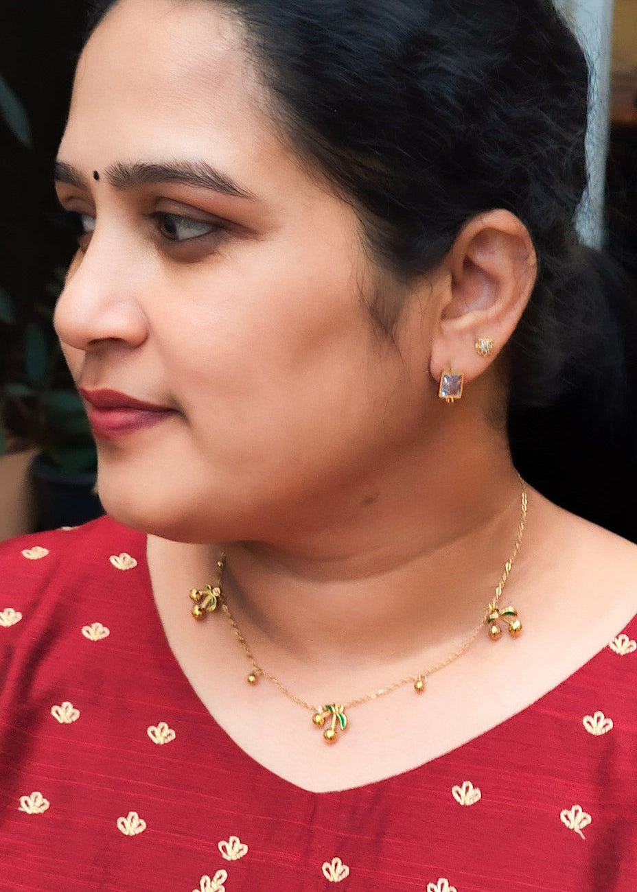 A woman in profile wearing a red embroidered top with a floral pattern at the bottom, along with a gold necklace and earrings.