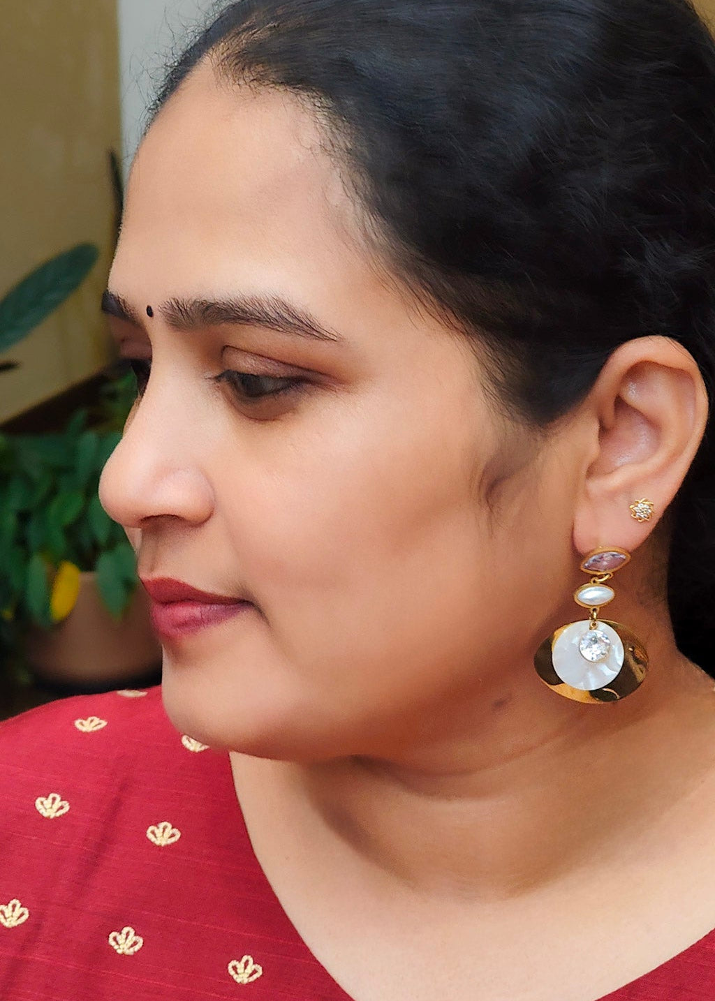 A woman wearing a prominent gold and white anti-tarnish teardrop earring.