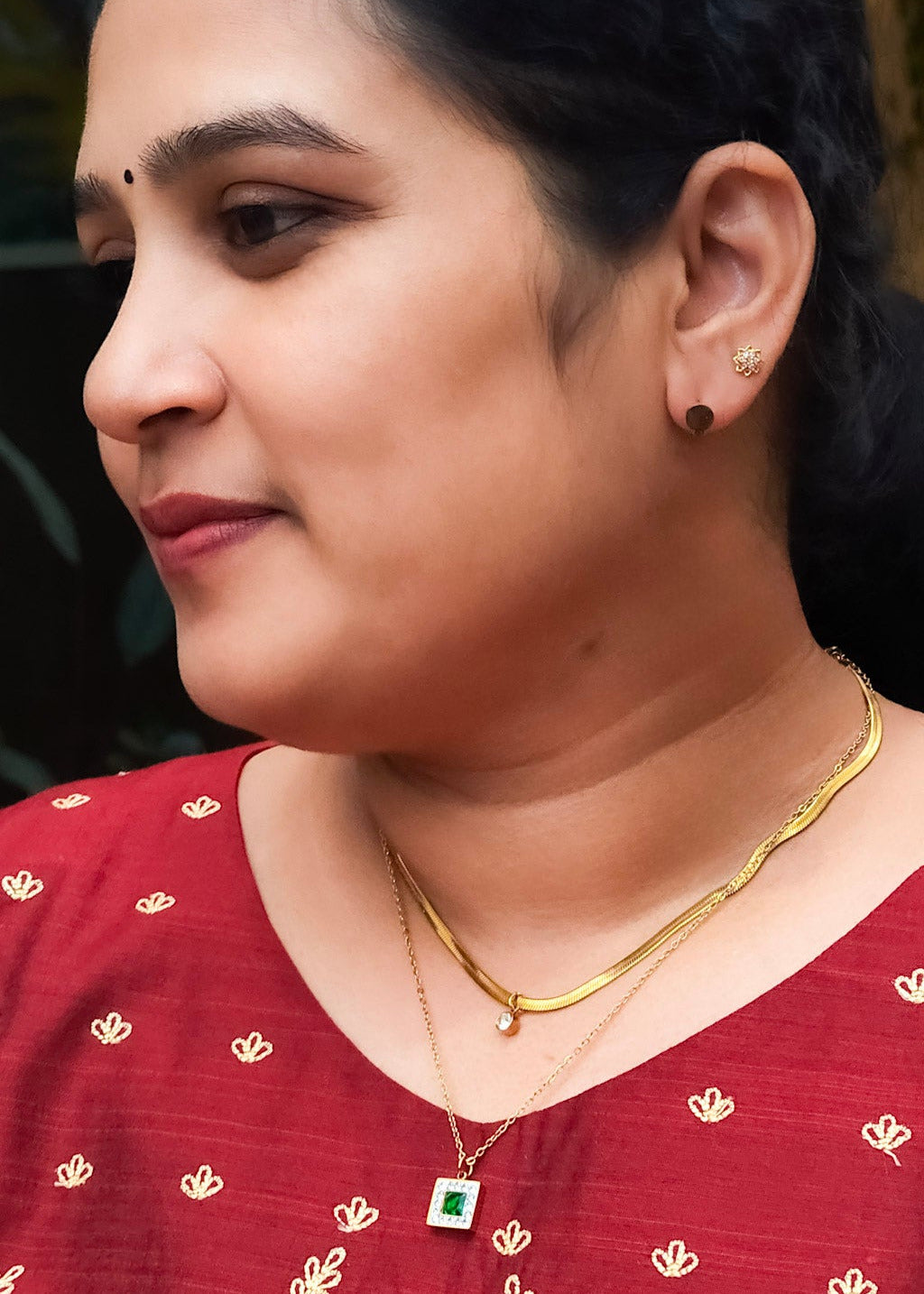 A close-up side profile of a woman wearing anti tarnish gold necklace with a green square pendant.
