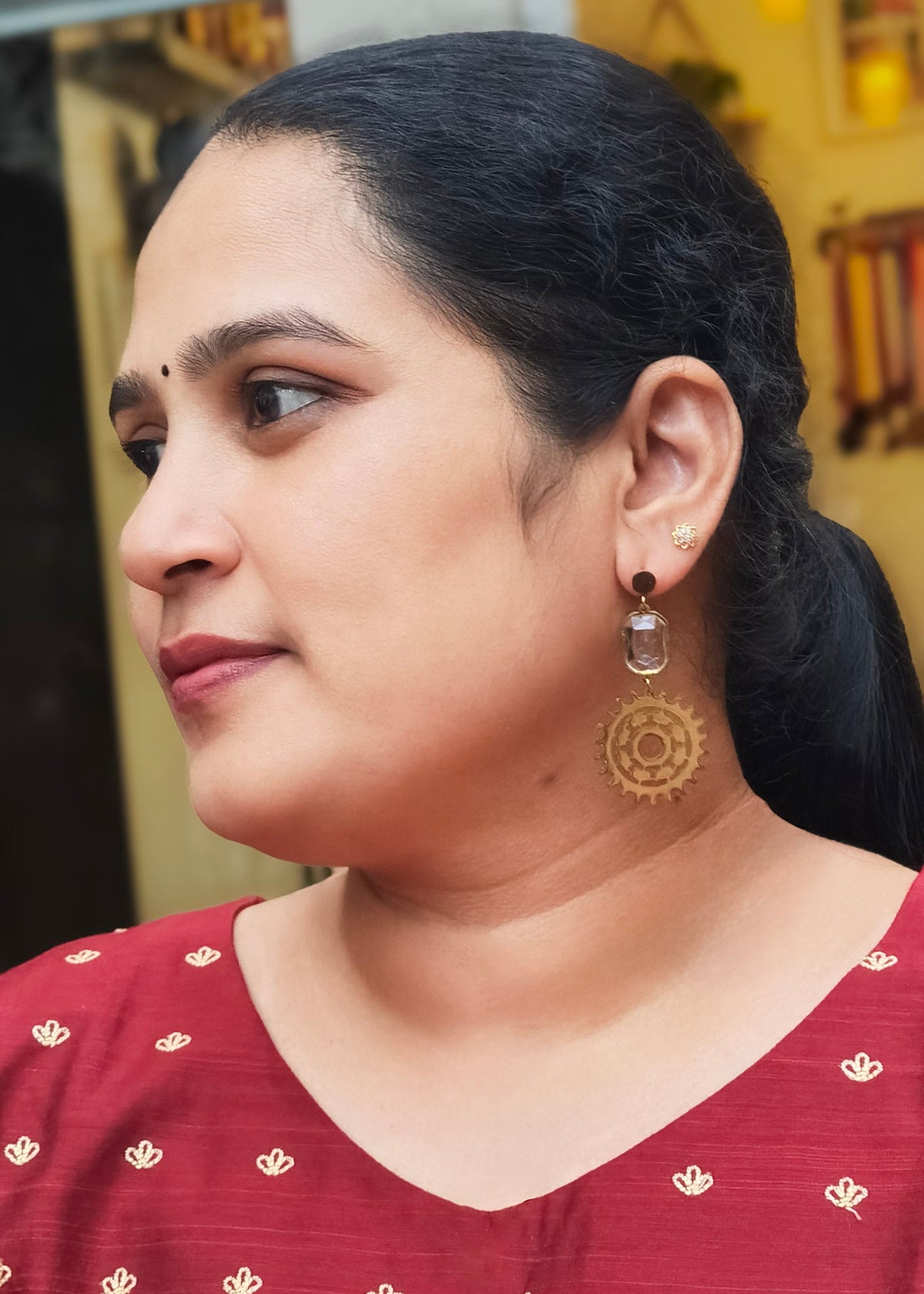 A woman wearing a gold-toned anti-tarnish dangle earring with a clear rectangular stone.