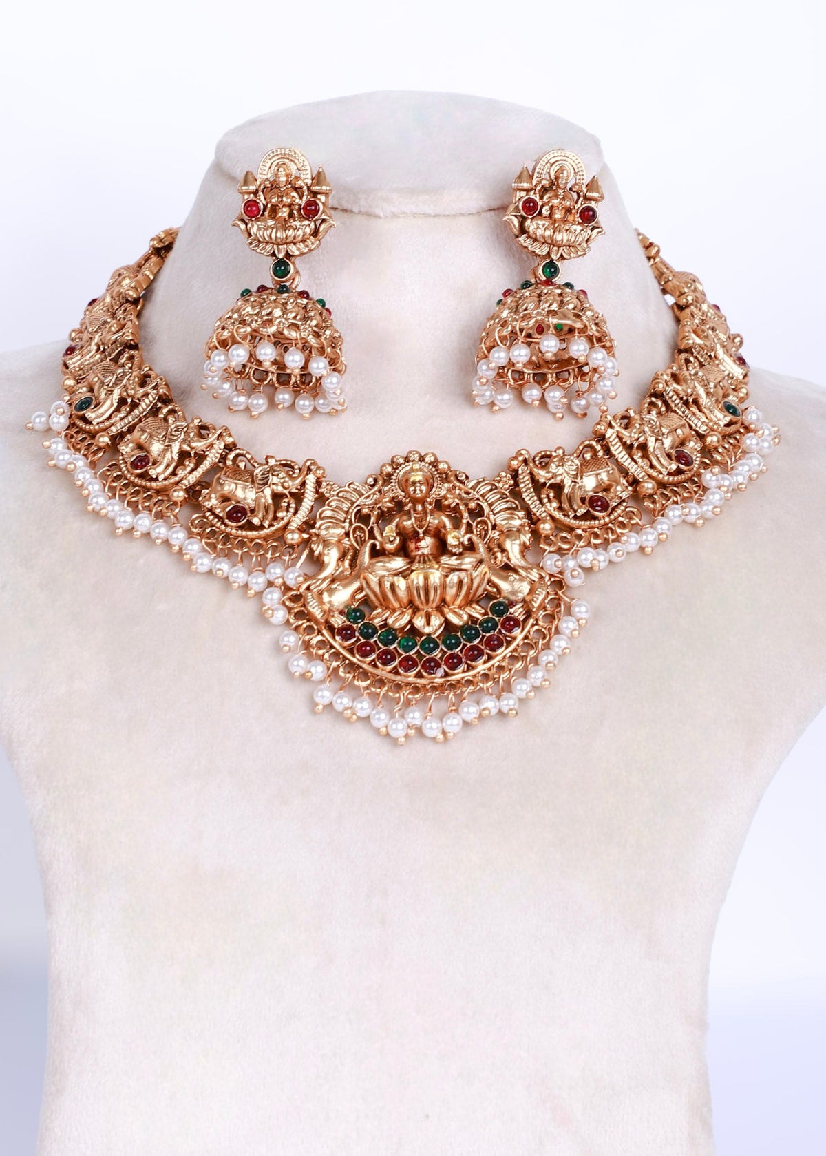 An ornate gold-toned traditional necklace and matching earrings displayed on a cream jewelry bust against a white background.