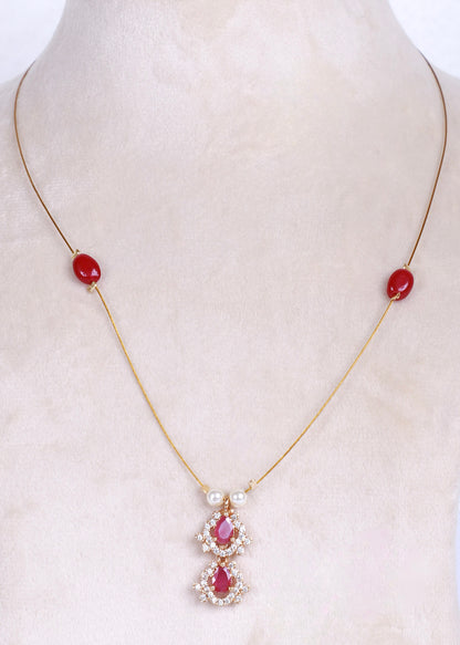 A gold chain necklace displayed on a cream-colored mannequin bust, featuring two small red oval beads on the chain and a central pendant with red teardrop-shaped stones surrounded by clear crystals.